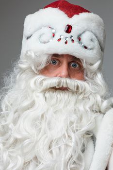 Stock photo of smiling happy Santa in traditional hat with rhinestones and long white beard looking at camera. Cutout on red background. Happiness concept.