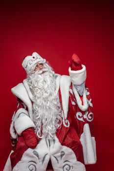 santa claus with long white beard shows something with his hand, picture isolated on red background