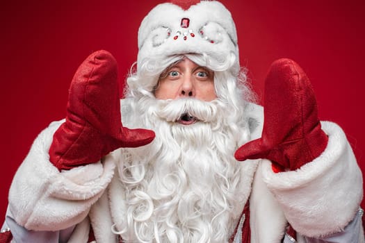 Santa Claus show size of something by hands in mittens with surprized face on red background, holiday emotions concept. High quality photo