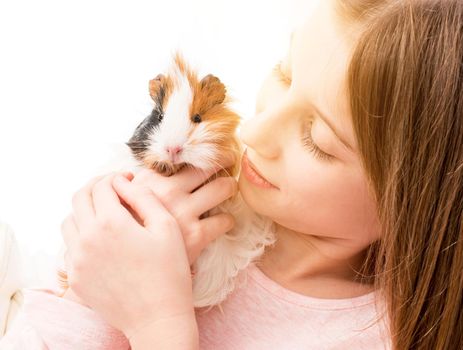 Charming little blonde girl holding guinea pig near her cheek and smiling