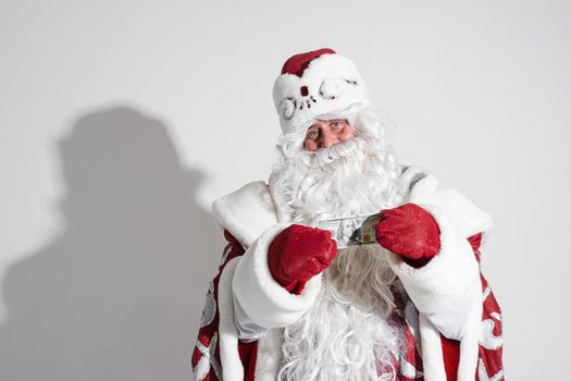 Smiling generous Santa Claus with long white beard in fancy costume holding banknote in hands wearing red mittens. Cutout on white background.