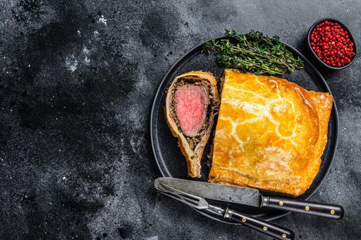 Beef Wellington classic steak dish with tenderloin meat on a plate. Black background. Top view. Copy space.