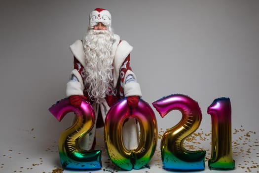 Santa Claus with colorful balloons in shape of 2021 on gray background with copy space, xmas and new year celebration. High quality photo