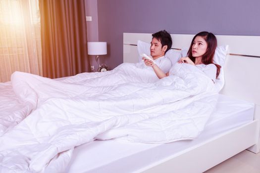 young couple lying on a bed with remote control of air conditioner in the bedroom