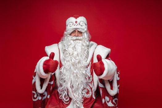 Stock photo of smiling Father Frost showing thumbs up and looking at camera. Isolate on red background.