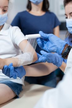 Closeup of african american pediatrician doctor bandage fractured broken arm of little patient during medical physiotherapy in hospital office. Young child having accident. Health care service