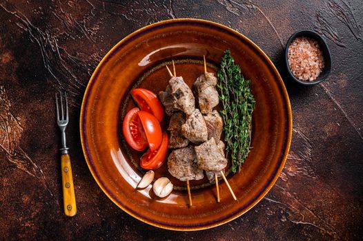 Bbq lamb meat on wooden skewers with vegetables on a rustic plate. Dark background. Top view.