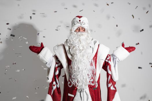 Santa in red traditional costume and white beard outstretching arms under falling silver confetti. Father Christmas congratulating with New Year.