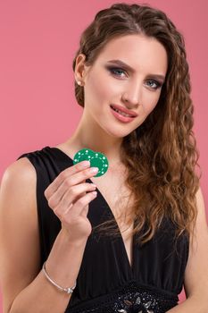 Portrait of a beautiful young woman with poker chips on pink background. Studio shot