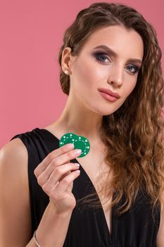 Portrait of a beautiful young woman with poker chips on pink background. Studio shot