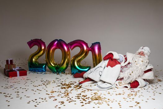 Stock photo of jolly Father Frost in festive clothing with long white beard outstretching his arms and smiling at camera under flying golden confetti. Isolated on grey background.