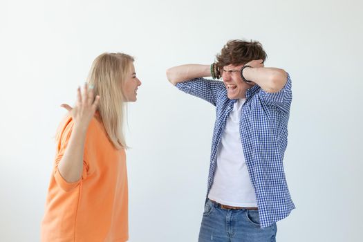 Young nervous couple wicked cute girl and upset young guy plugging ears cursing standing against white background. Misunderstanding and relationship crisis concept