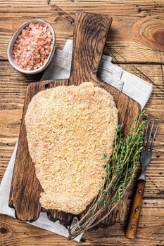 Tender Raw Breaded Wiener schnitzel on a wooden board with thyme. wooden background. Top view.