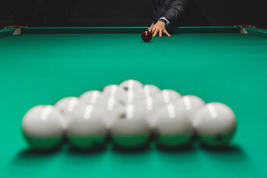 Focus on the hand of a man in a suit aiming for a kiy in a pile of white billiard balls. Draw of the right of the first blow.