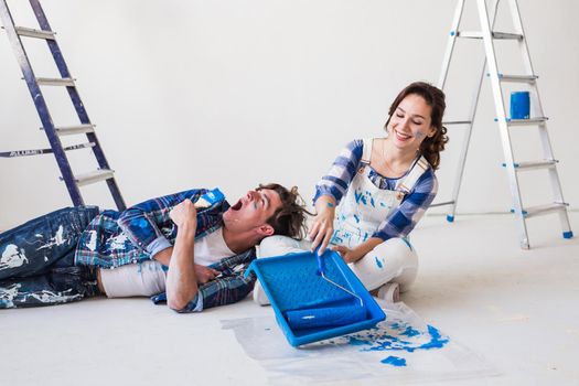 Smiling loving couple doing home renovations, the woman is holding a paint roller and young man is resting.