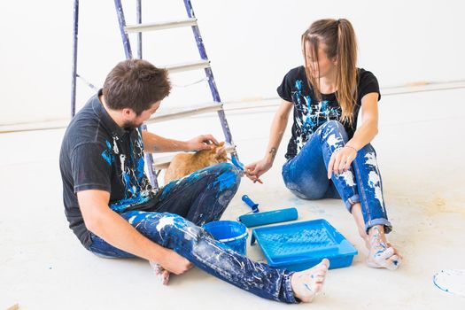 Pet, redecoration and relationship concept - Young funny couple with cat doing renovation in new apartment.