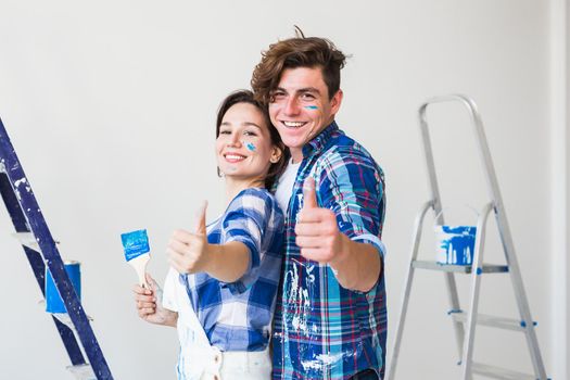 Redecoration, renovation and love couple concept - young man and woman in love and painting the wall, showing thumbs up.