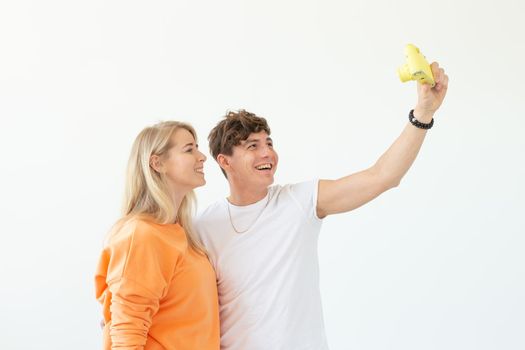 Funny crazy young couple blonde girl and a hipster guy taking a selfie on a vintage yellow film camera posing on a white background. Concept of photography hobby. Advertising space