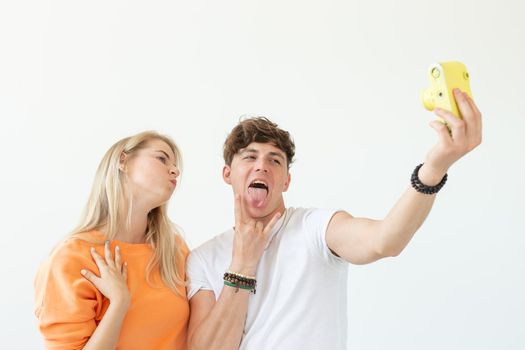 Funny crazy young couple blonde girl and a hipster guy taking a selfie on a vintage yellow film camera posing on a white background. Concept of photography hobby. Advertising space