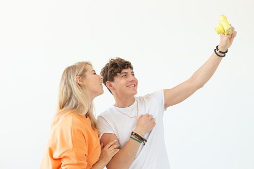 Funny crazy young couple blonde girl and a hipster guy taking a selfie on a vintage yellow film camera posing on a white background. Concept of photography hobby. Advertising space