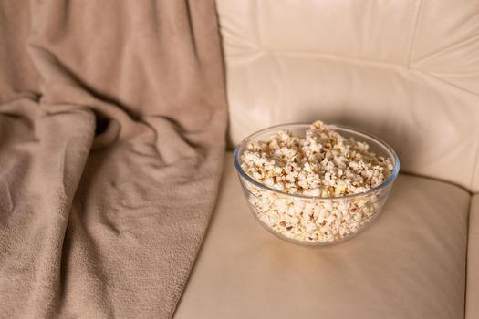 Bowl of popcorn for watching a film on a beige couch. Snacks and unhealthy junk food.