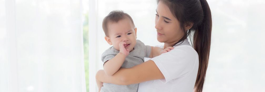 Young asian mother holding little baby girl and walking together in the bedroom at home, mom carry daughter and care, relationship of parent and child, toddler and parent, indoor, family concept.