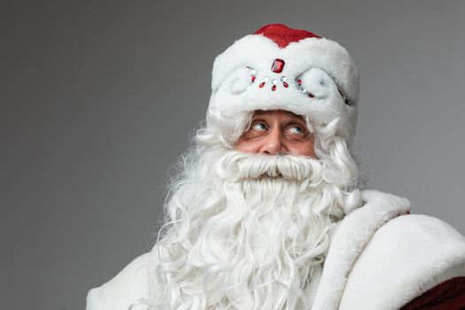 Stock photo portrait of aged man wearing traditional Father Frost costume with winter hat decorated with rhinestones and white long beard. Father Frost looking up with doubt face.