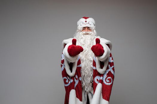 Stock photo of calm Father Frost with long white beard in traditional red and white costume holding both thumbs up.