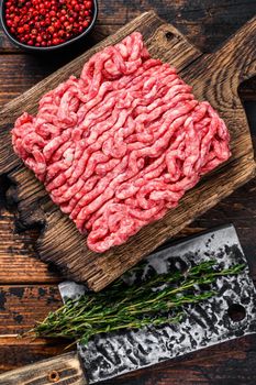 Raw mince beef, ground meat with herbs and spices on a wooden cutting board. Dark wooden background. Top view.