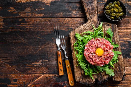 Tartar beef with a quail egg and arugula served on a cutting board. Dark wooden background. Top view. Copy space.
