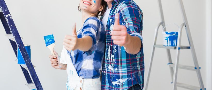 Redecoration, renovation and love couple concept - young man and woman in love and painting the wall, showing thumbs up.