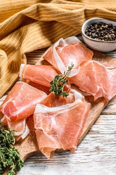 Spanish jamon Serrano on a cutting board, cured ham. White wooden background. Top view.