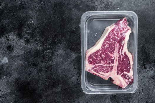 T-bon raw beef steak in vacuum packaging. Black background. Top view. Copy space.