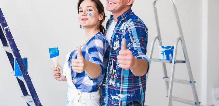 Redecoration, renovation and love couple concept - young man and woman in love and painting the wall, showing thumbs up.