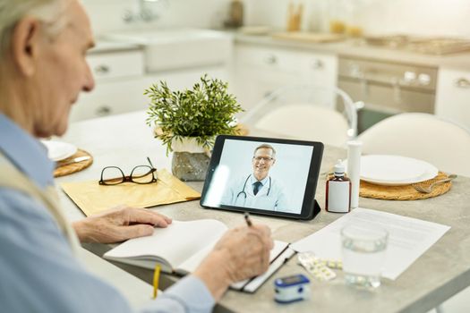 Fragment photo of eldelry gentleman contacting his family doctor online with the help of wireless tablet