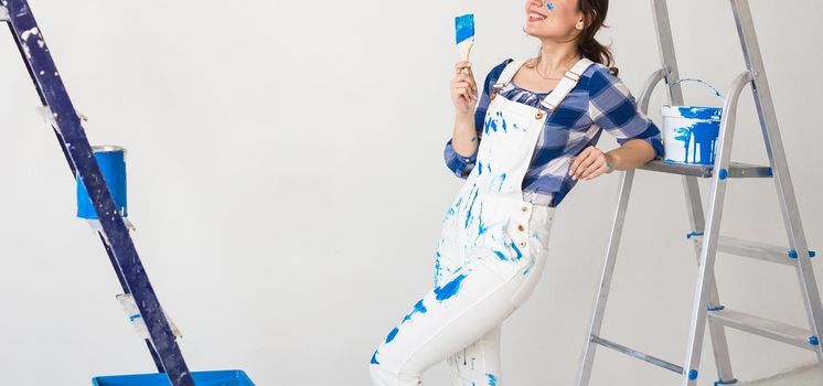 Repair, renovation, new home and people concept - close up of young woman doing redecoration over white wall.