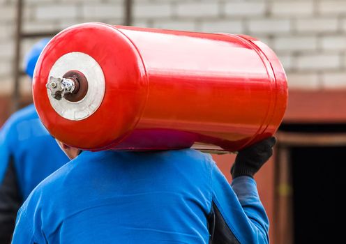 A male industrial worker walks with a gas cylinder to a gas car. Transportation and installation of a propane bottle to residential buildings.