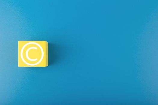 Minimal trendy copyright, intellectual property and patenting concept. Copyright symbol on yellow block against blue background with copy space