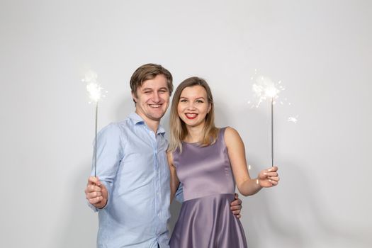 Holidays, party and celebrations concept - young couple with sparklers on white background.