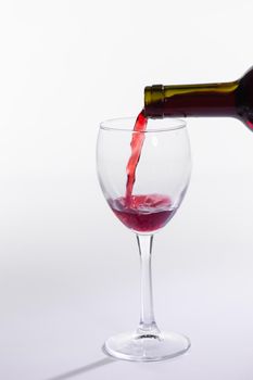 Red wine pouring into glass from bottle on white background.