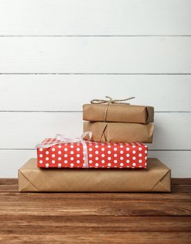 Close up stack of several red and brown paper wrapped gifts on wooden table over white wall