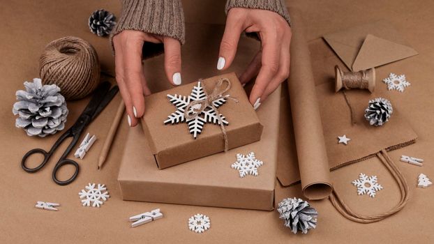 Close up woman hands packing and wrapping Christmas gift boxes in natural brown paper, high angle view