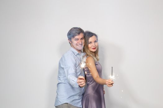 Holidays, party and celebrations concept - young couple with sparklers on white background.