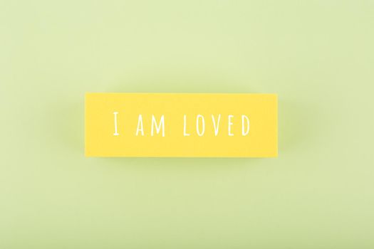 I am loved written on yellow rectangle in the middle of bright green background. Concept of positive motivational quotes for kids and adults