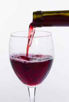 Pouring red wine into the glass on white background.