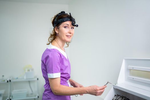 Profession medical industry. Portrait of woman ENT doctor posing in office before examining patient. Physician in bright colored uniform with medical equipment and tools for ENT practice in hospital.