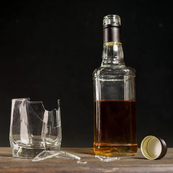 Broken glass and a bottle of whiskey. The concept of ruined life due to alcoholism. - image