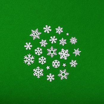 Close up circle of white wooden snowflakes Christmas decoration over green felt background, table top view, flat lay