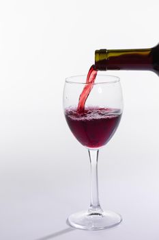 Red wine pouring from bottle into big glass on white background.