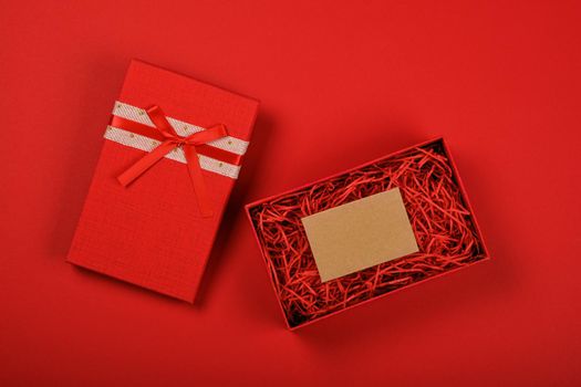 Valentine template of one open red gift box with ribbon bow and white paper note on red background, close up flat lay, elevated top view, directly above